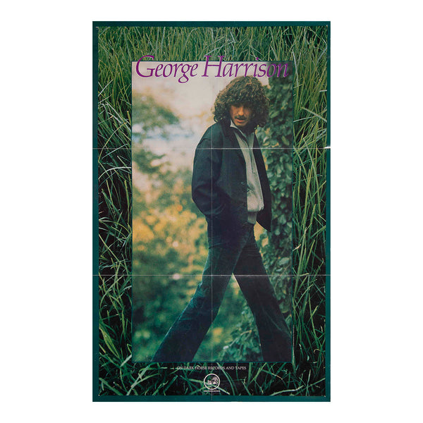 A vintage-style poster or print featuring a portrait of George Harrison standing in tall grass, with his name in purple text at the top and a dark border around the artwork.